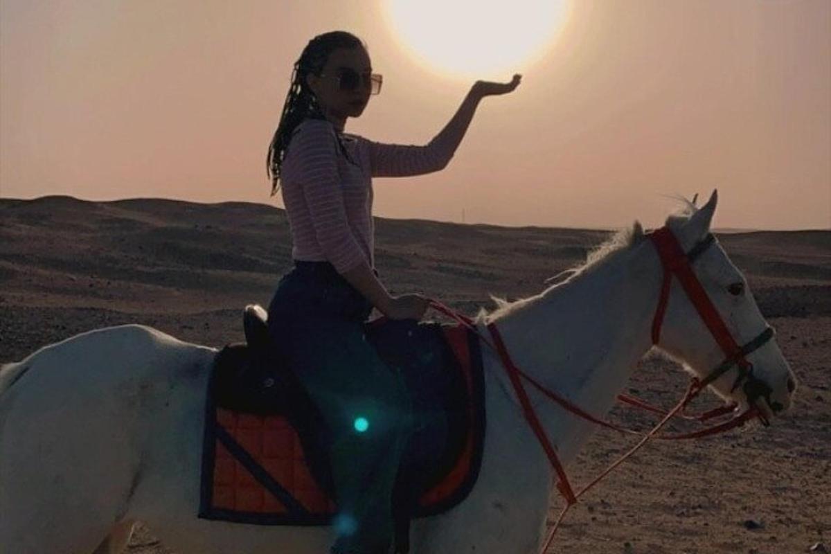 uma jovem cavalgando um cavalo branco no deserto