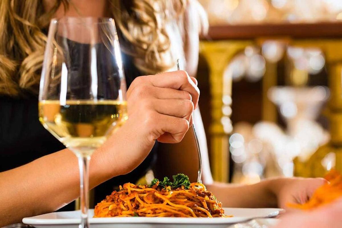 Una mujer comiendo espaguetis con una copa de vino.