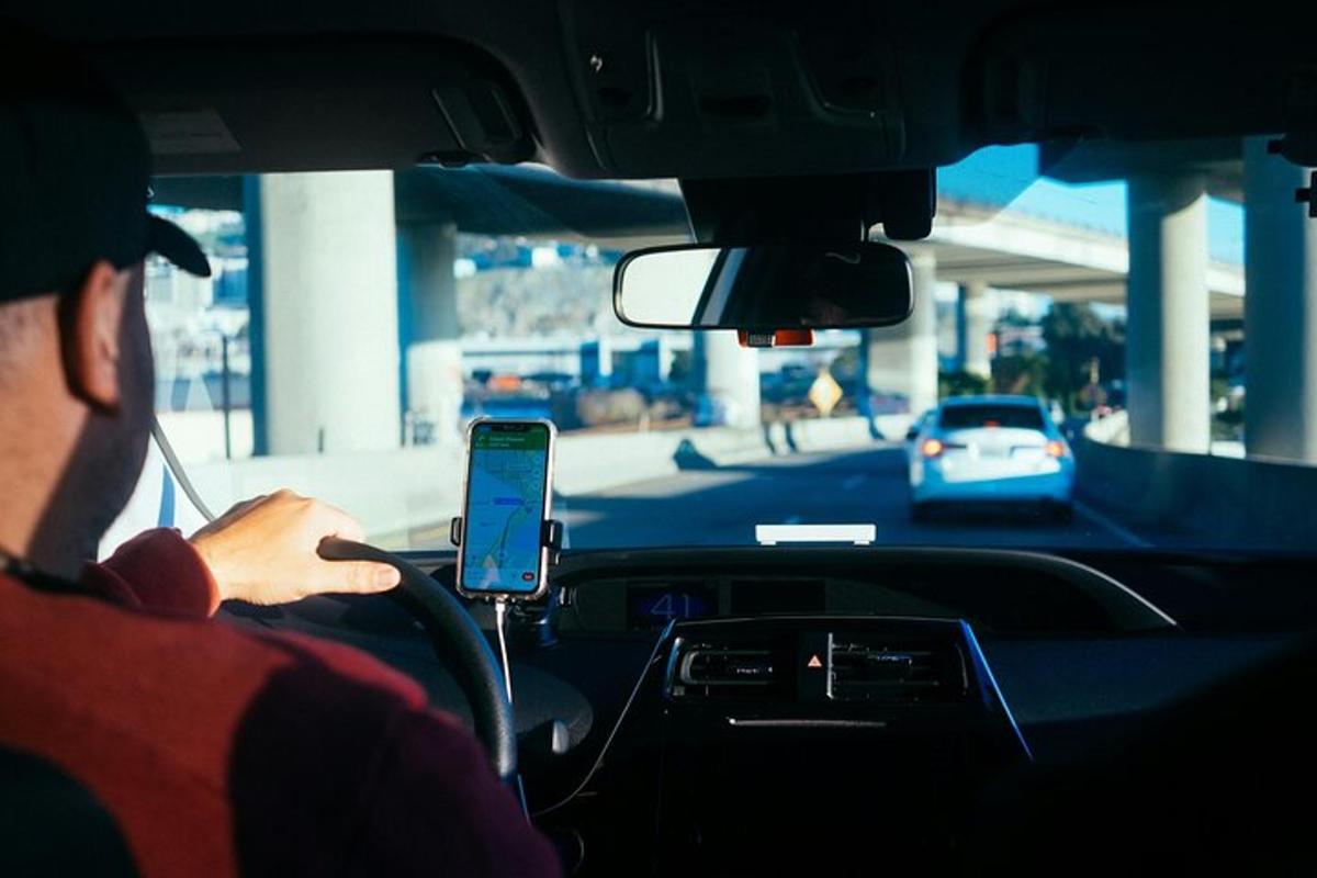 muž šoféruje auto a pozerá sa do mobilného telefónu