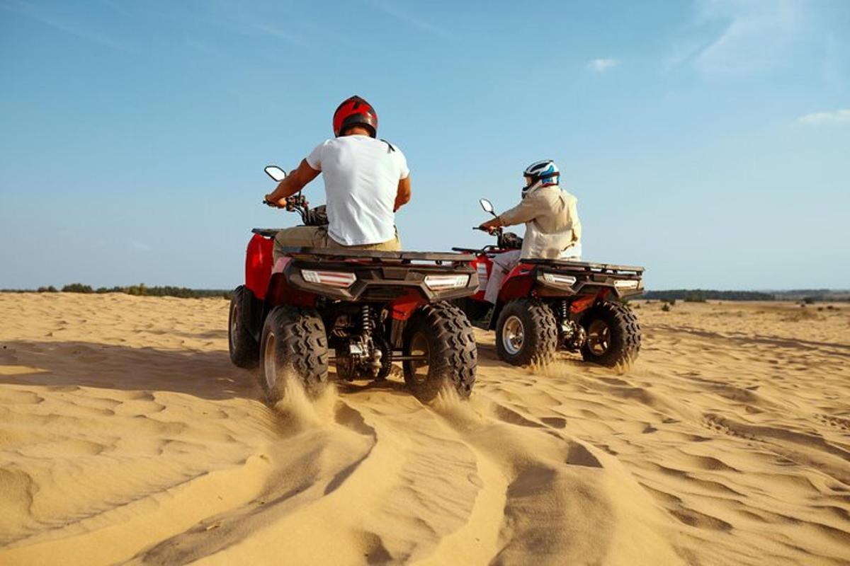 două persoane care călătoresc pe ATV-uri pe nisip
