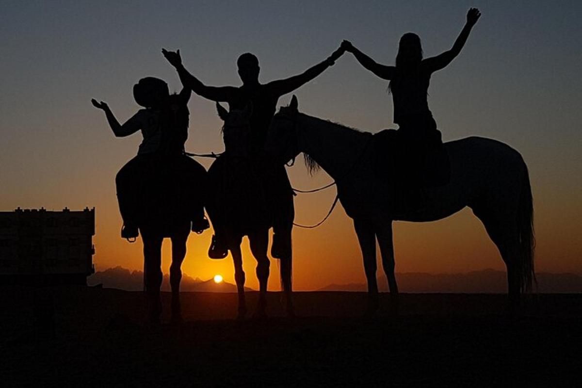 a group of three people riding horses at sunset