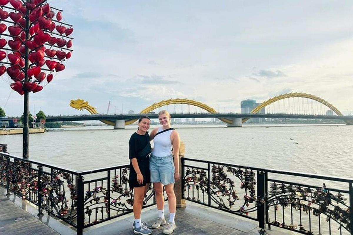 două femei stând lângă un râu cu un pod în fundal