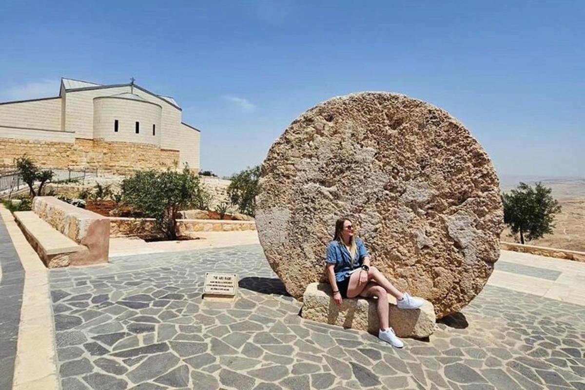 a woman sitting on a bench in front of a large rock
