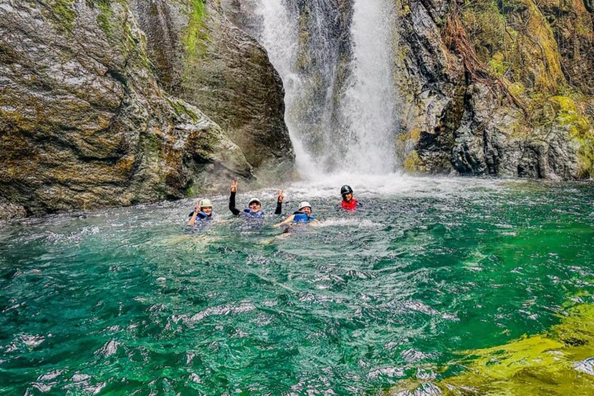three people in the water in front of a waterfall