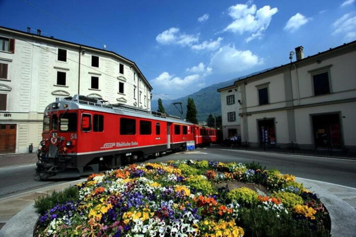 un tren vermell que circula per un carrer al costat d'edificis