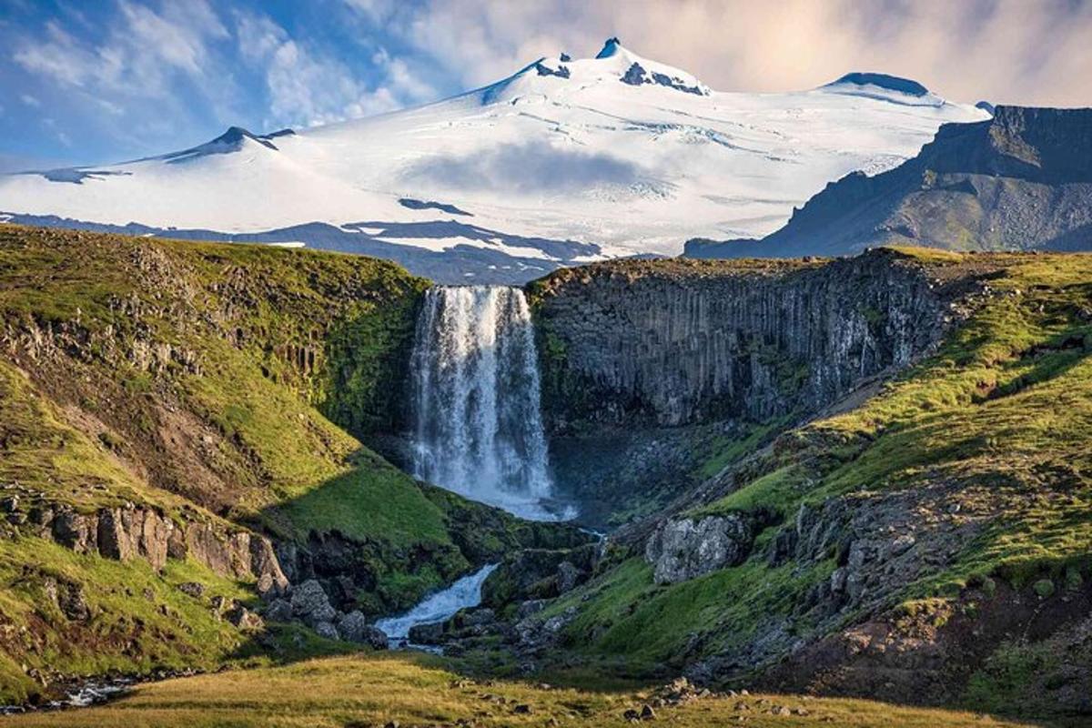 a snow capped mountain with a waterfall in a valley
