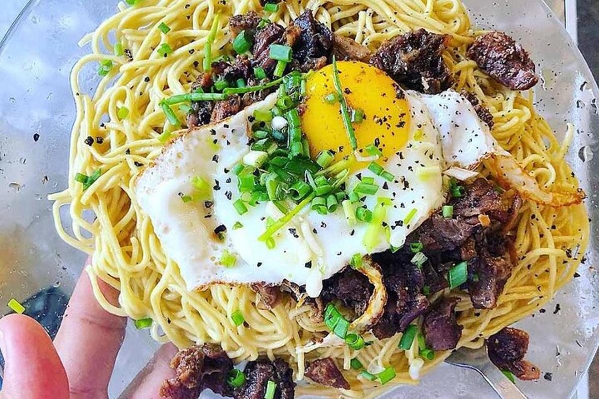 egy személy, aki egy tányér spagettit tart a kezében, tetején tojással