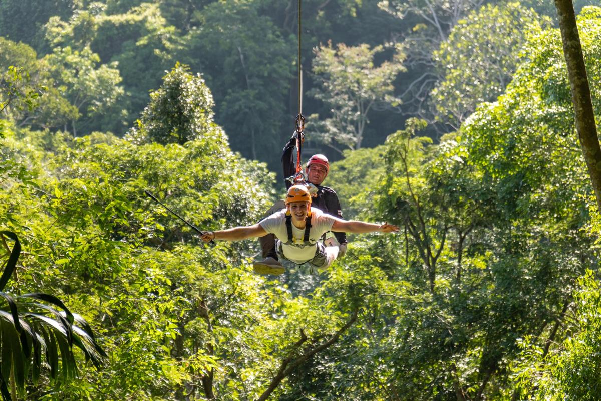 dva lidé se projíždějí na zipline mezi stromy v džungli
