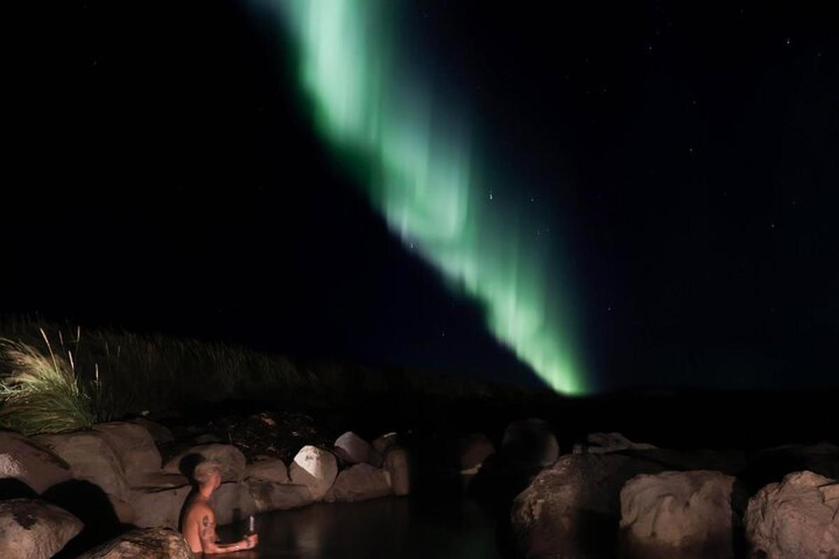una persona seduta sulle rocce sotto l'aurora boreale
