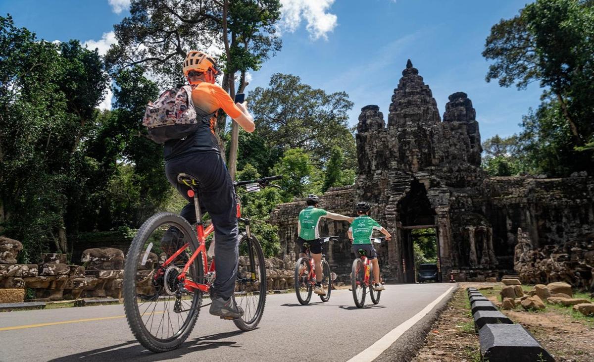 two people riding bikes down a road in front of a building