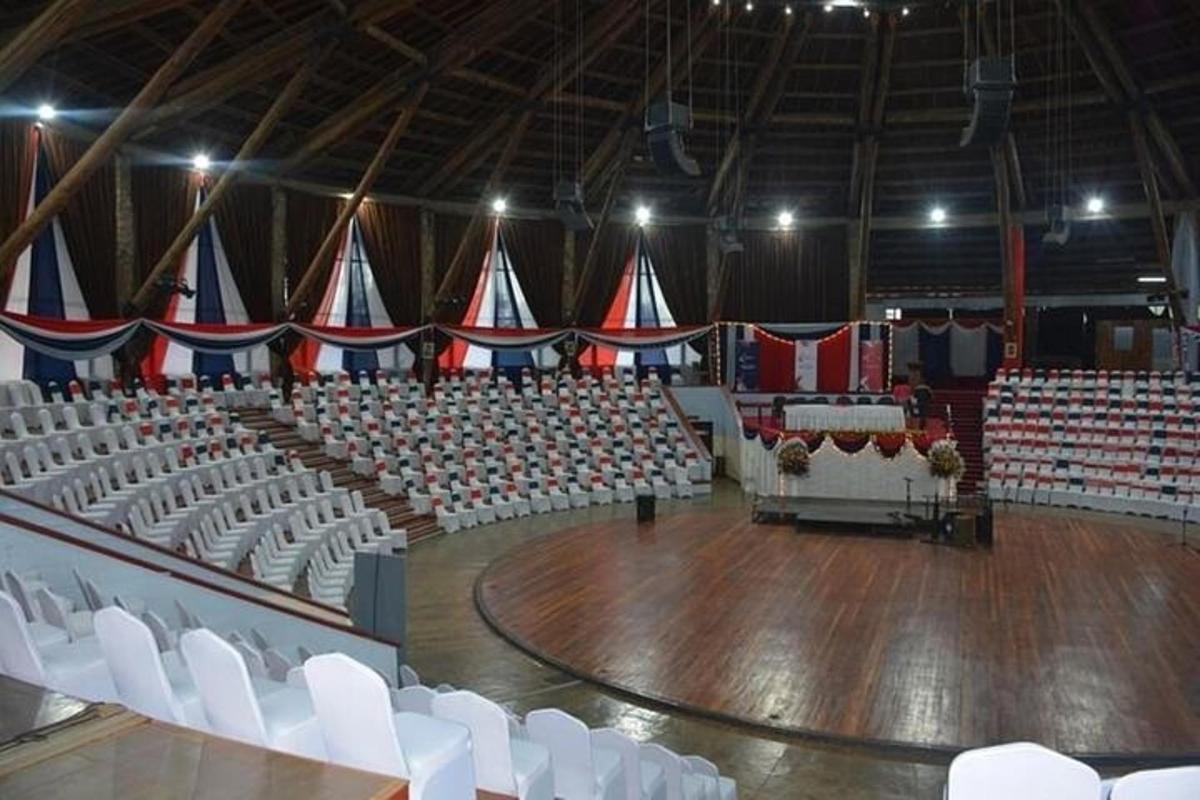Un auditorio vacío con sillas blancas y piso de madera.