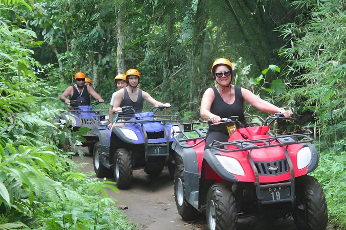 tiga orang mengendarai ATV di jalan setapak di hutan