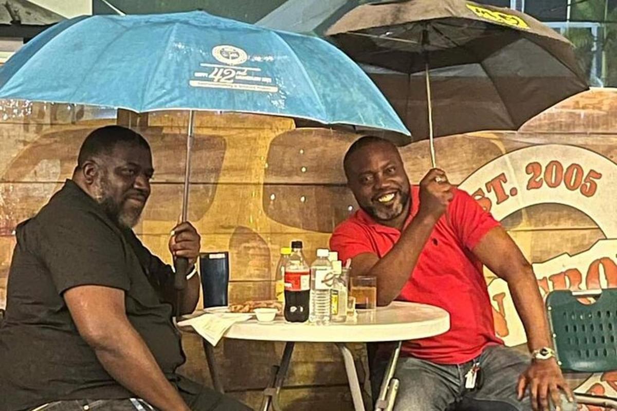 Dos hombres sentados en una mesa bajo una sombrilla