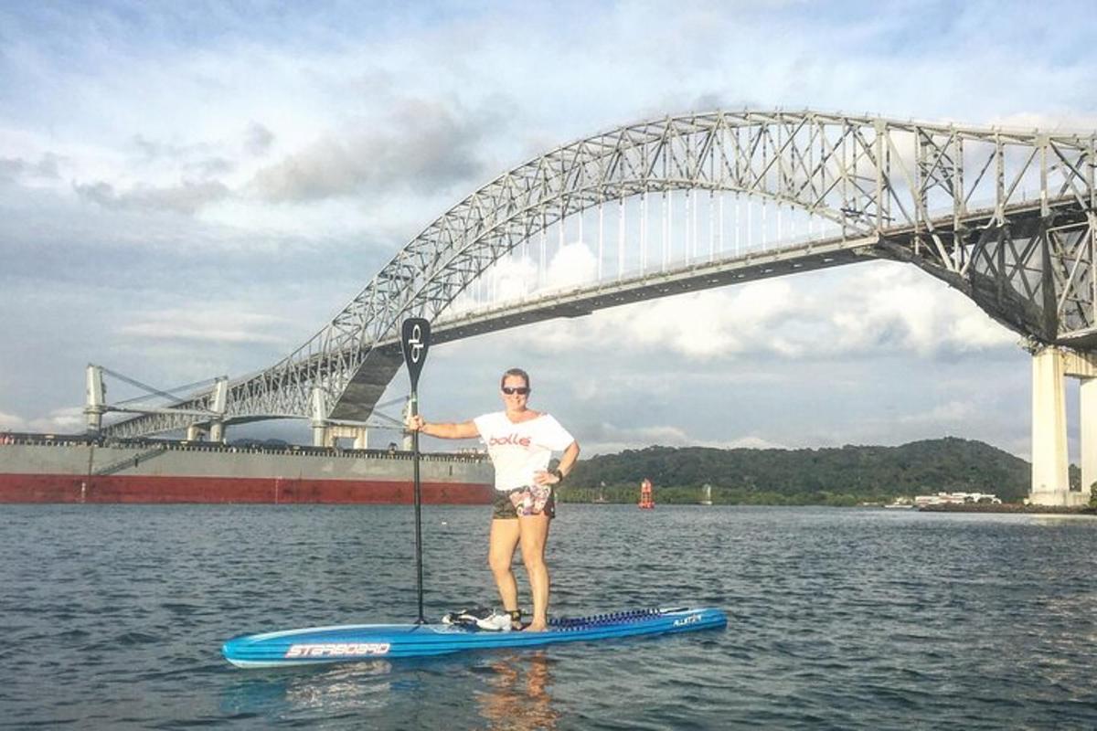 een man op een paddleboard in het water voor een brug