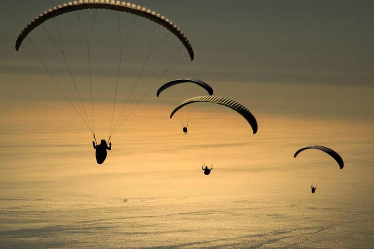 Tři lidé seskočí padákem na obloze nad oceánem