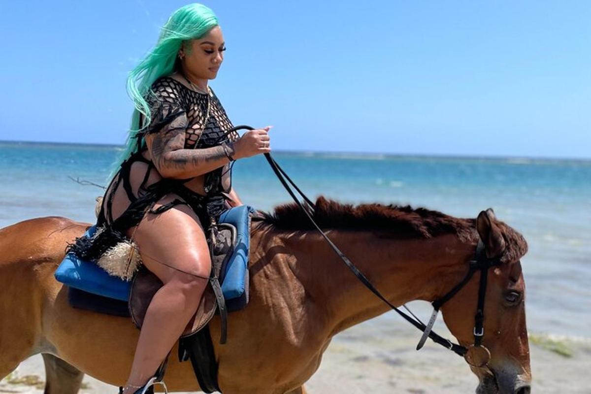 una donna con i capelli verdi a cavallo sulla spiaggia
