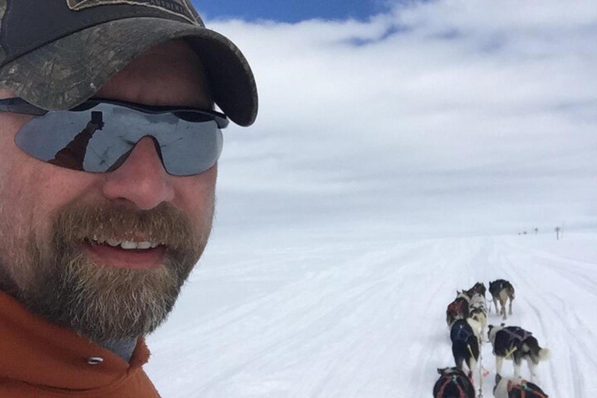 un uomo con occhiali da sole e barba e un gruppo di cani nella neve