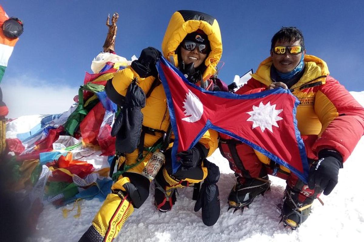 two people sitting on the snow holding a flag