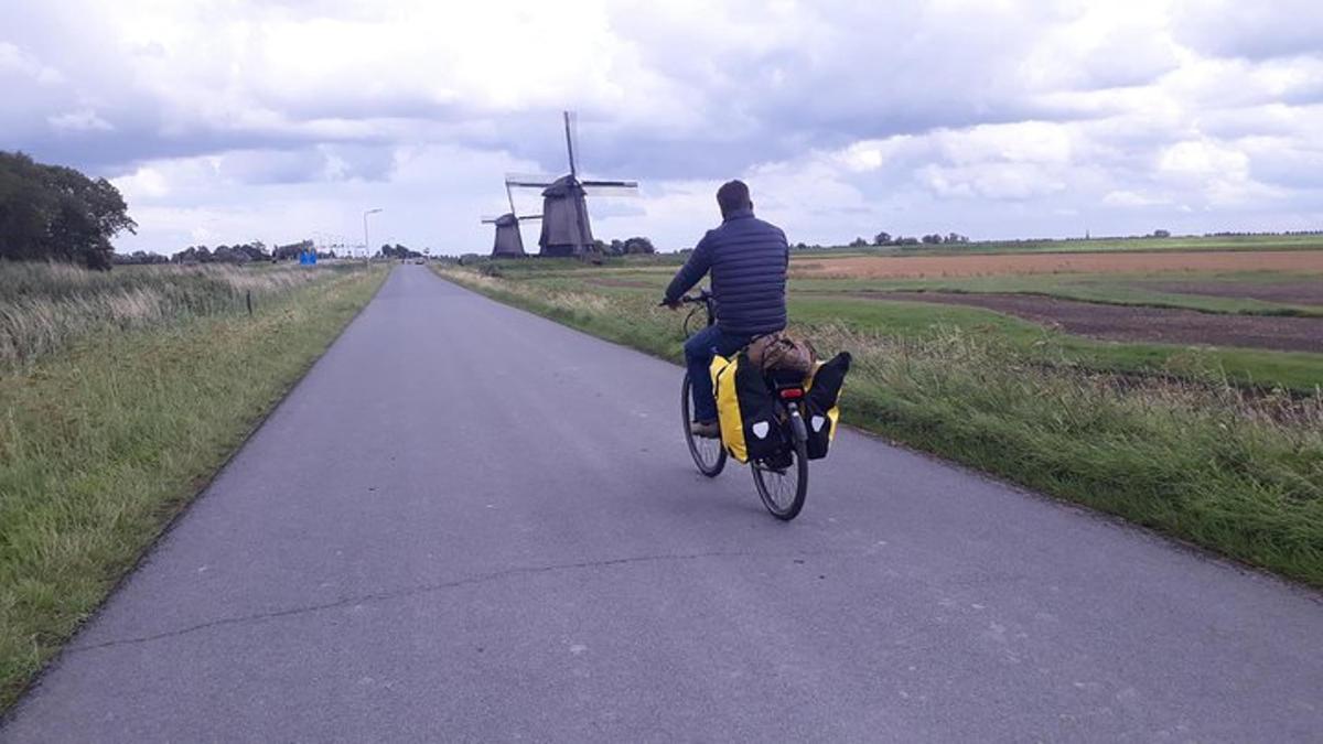 un home anant en bicicleta per una carretera amb un molí de vent