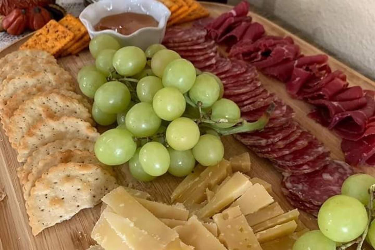 Un plato con uvas, queso y otros tipos de carnes.