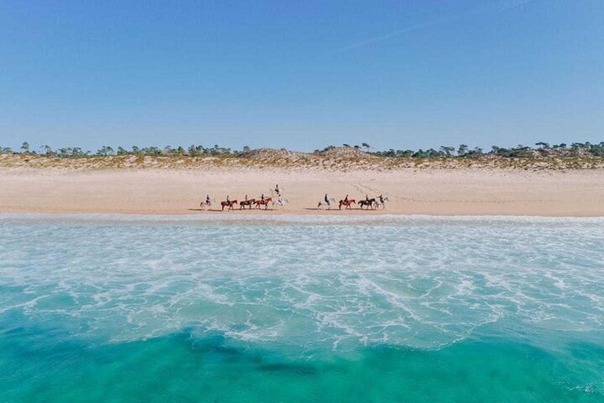 un grup de persones muntant a cavall a la platja
