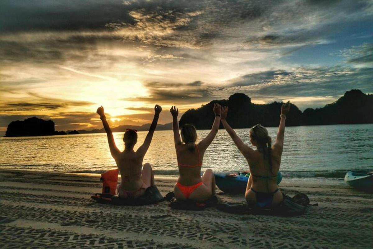 Tres mujeres sentadas en la playa con las manos en el aire