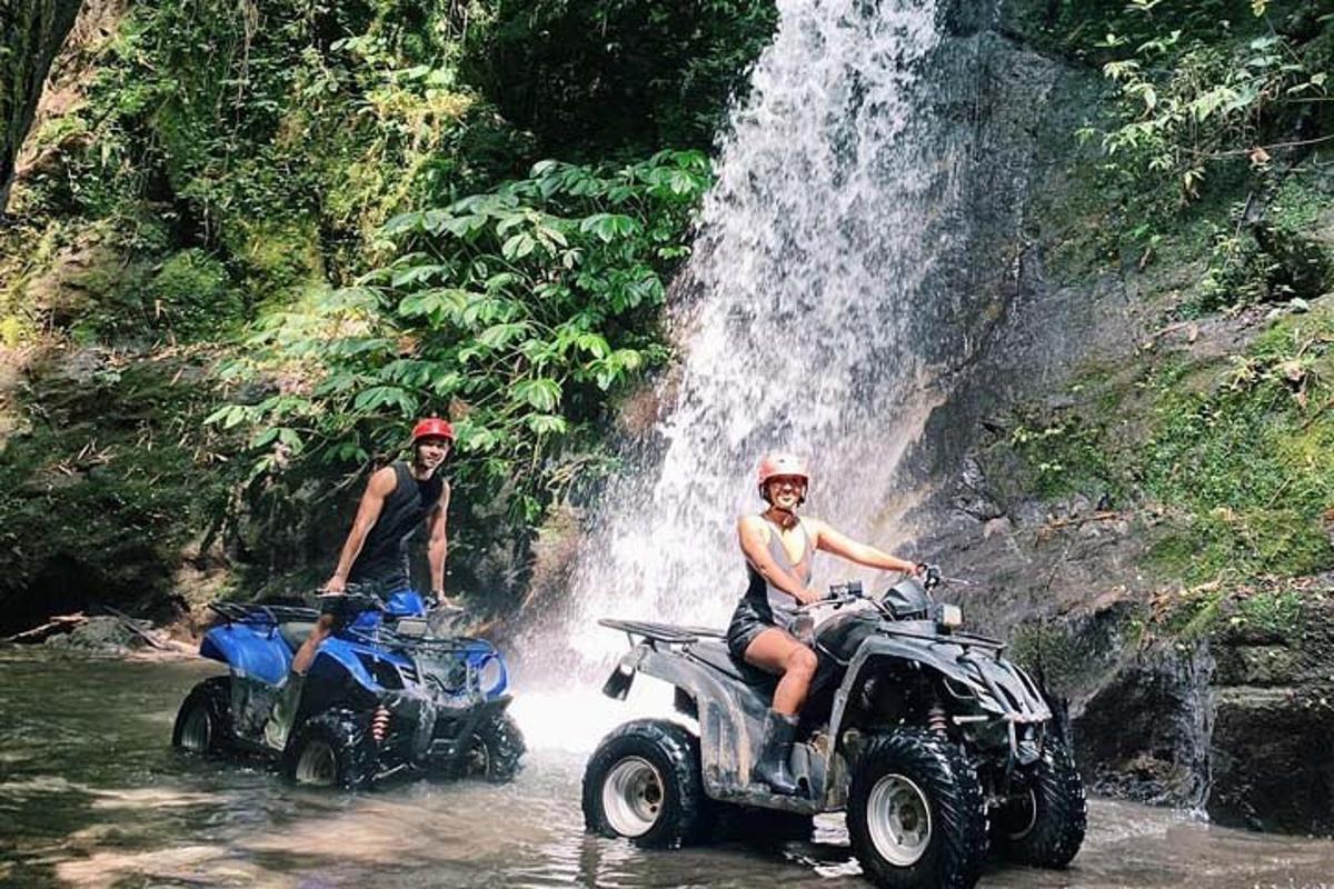 duas pessoas em quadriciclos na água perto de uma cachoeira