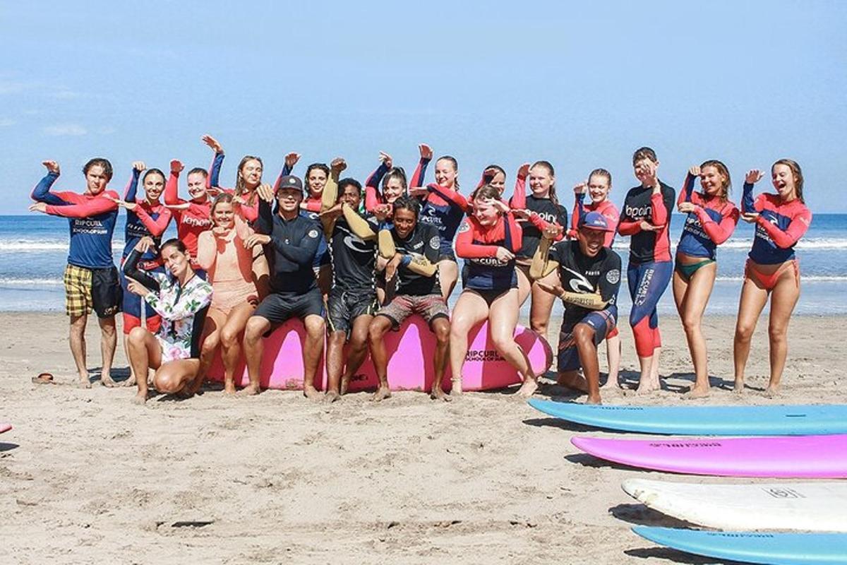 en gruppe mennesker som poserer på et rosa surfebrett på stranden