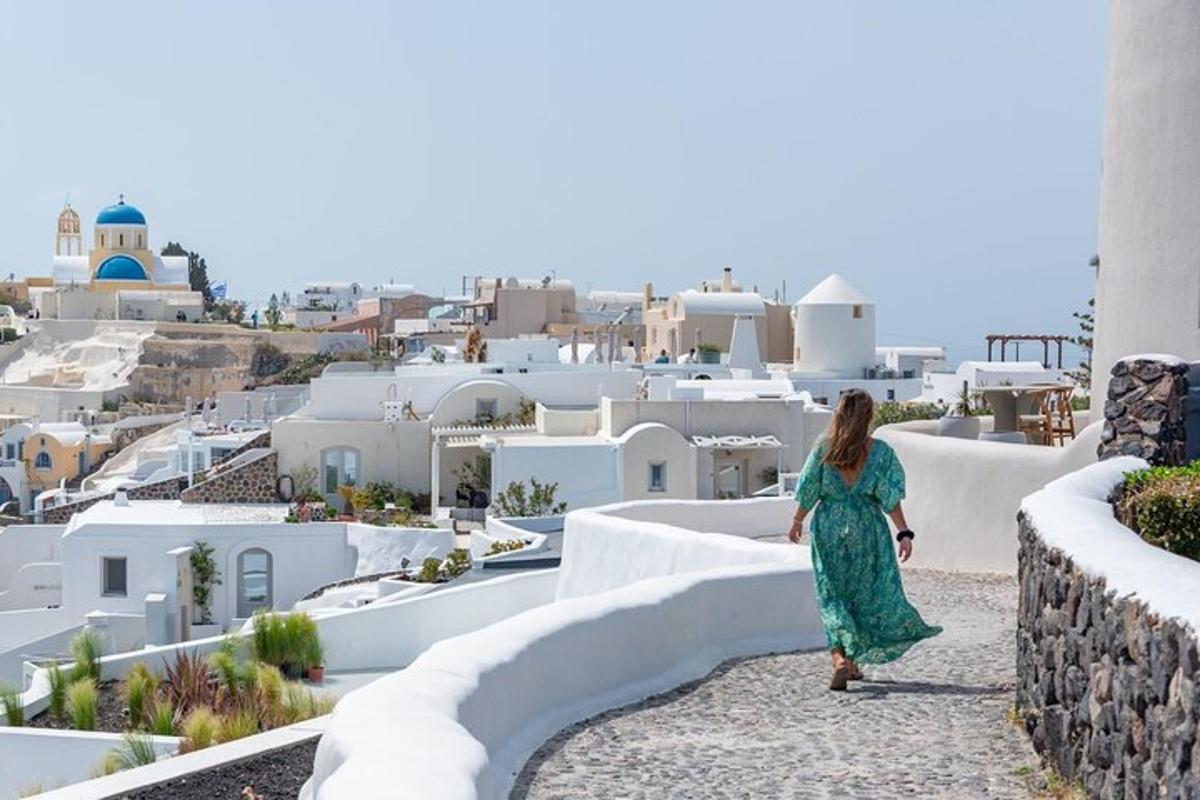 una dona amb un vestit verd caminant per un camí amb vistes a edificis blancs
