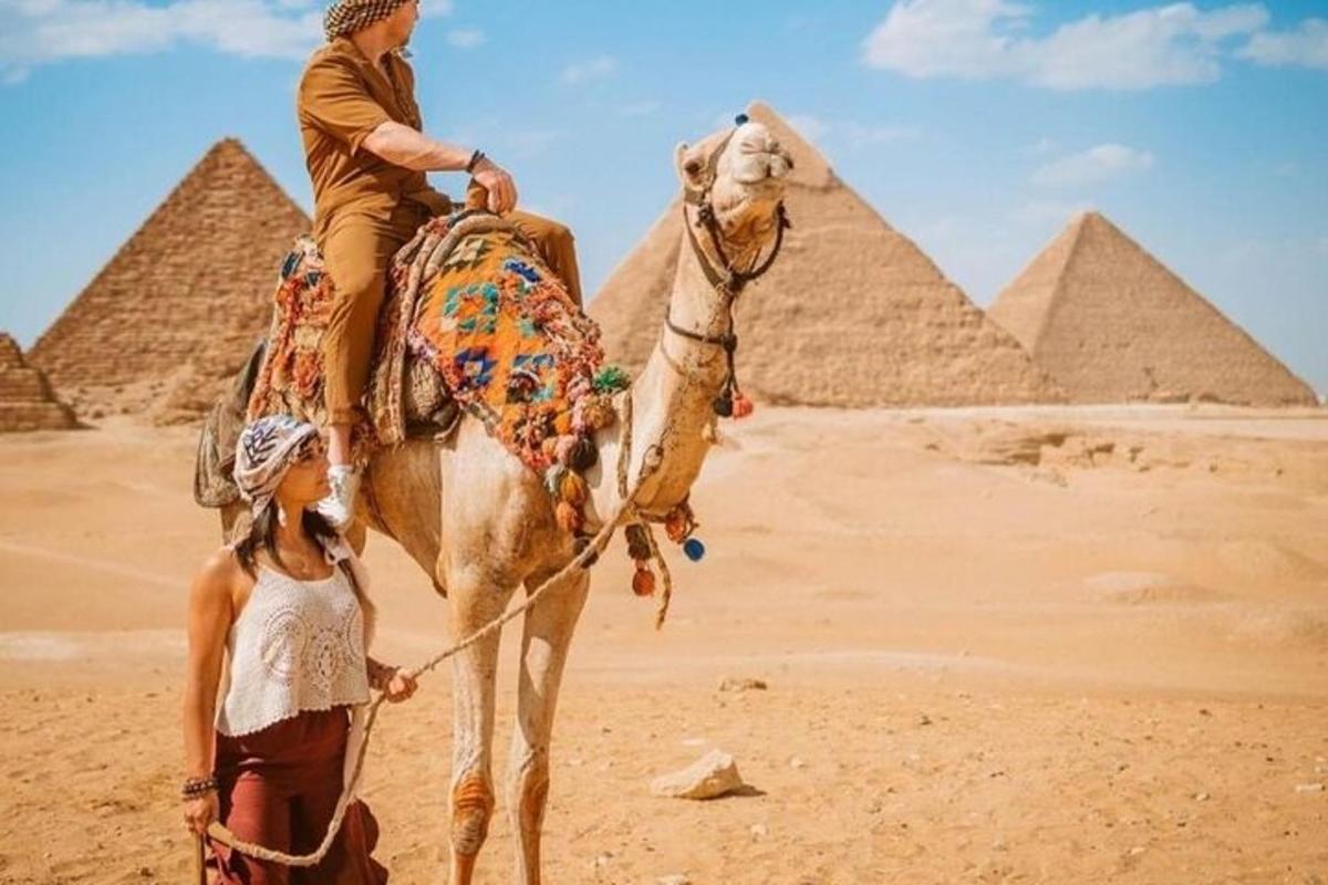 muž jedoucí na velbloudovi před pyramidami