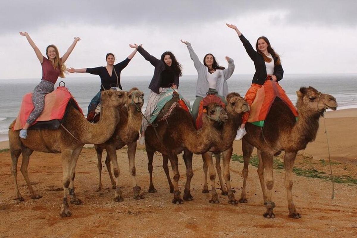 eine Gruppe von Frauen, die auf Kamelen am Strand reiten