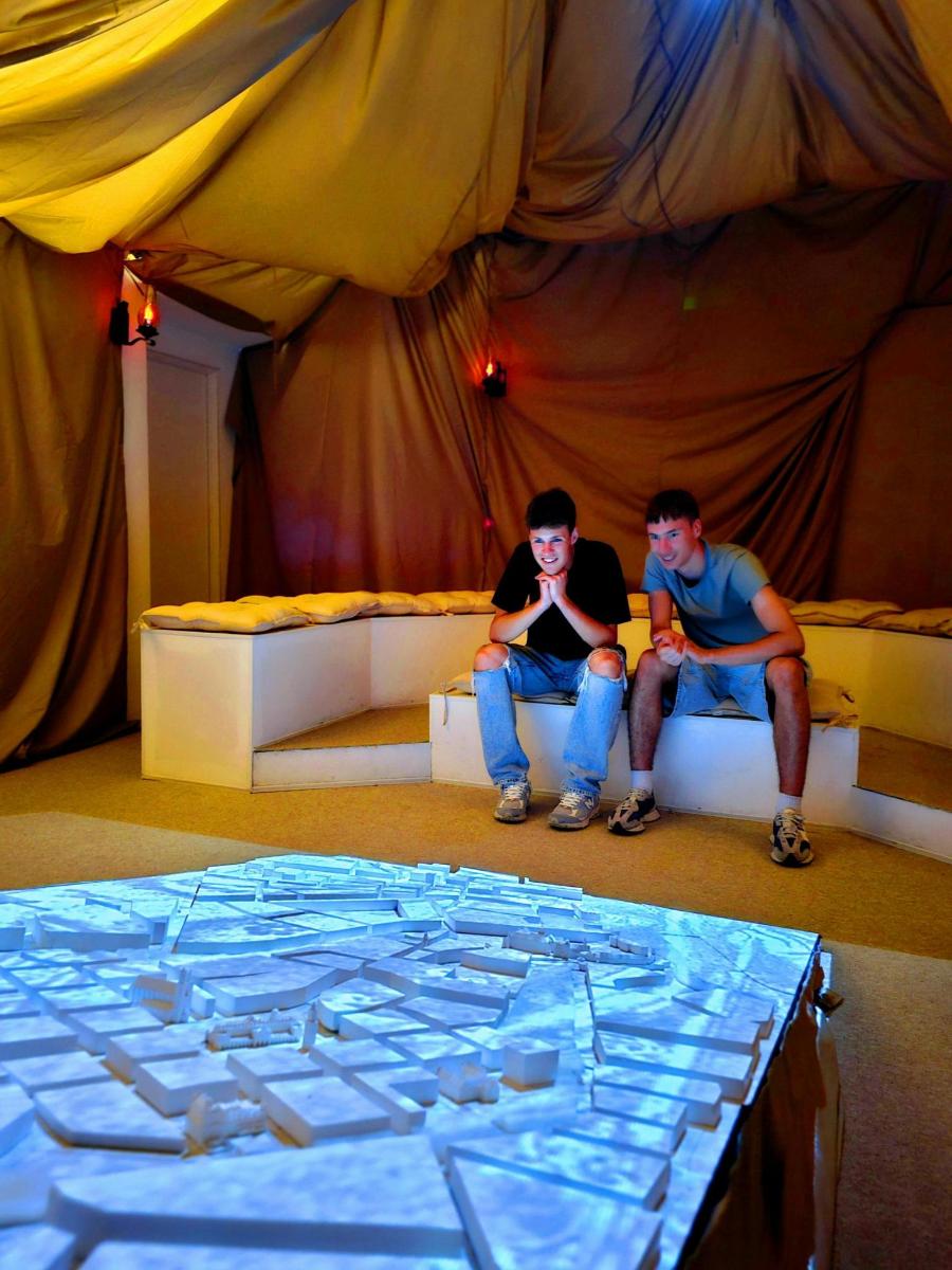 two men sitting on couches in a stage with a large table