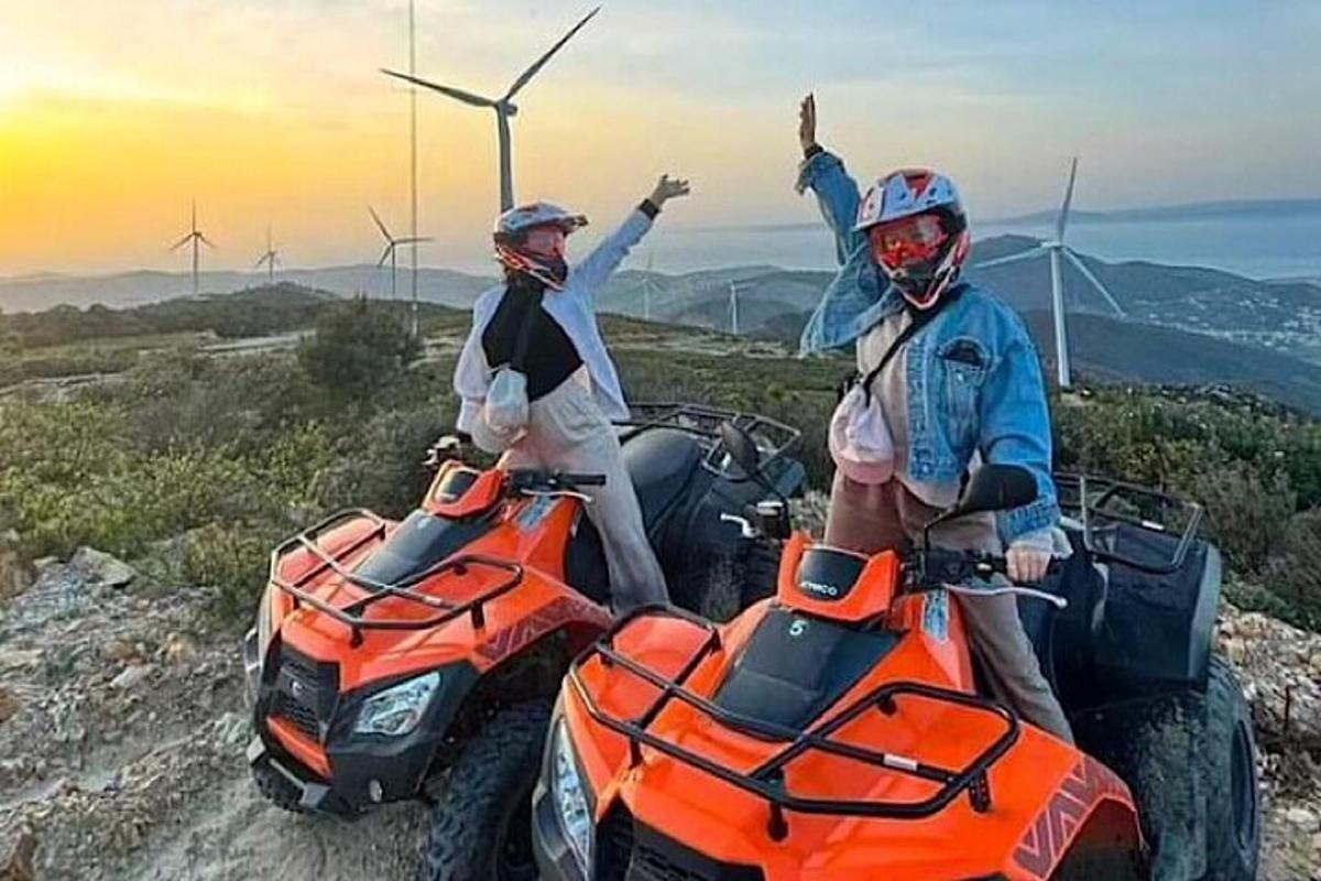 Dos personas en vehículos todo terreno en una montaña con turbinas eólicas