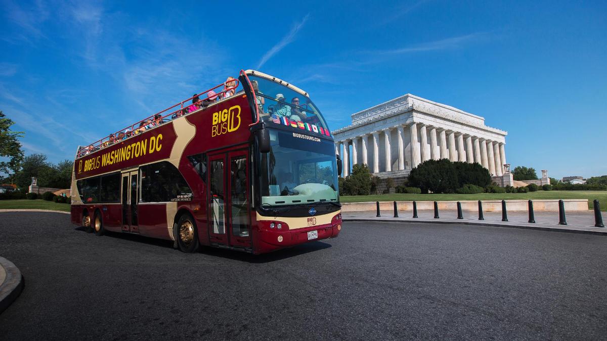 a red double decker bus driving past a building