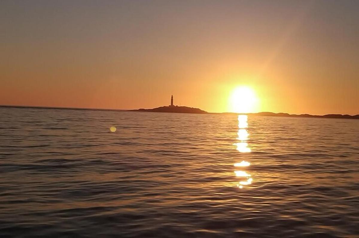 a sunset on the water with a lighthouse in the distance