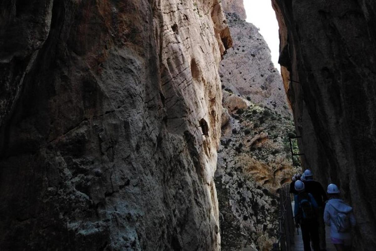 two people walking down a narrow path in a mountain