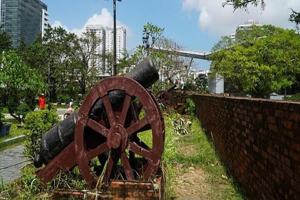 um canhão enferrujado sentado ao lado de uma parede de tijolos