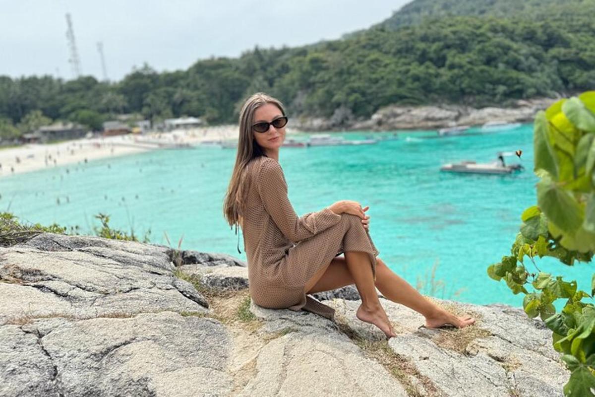 una mujer sentada en una roca junto a una playa