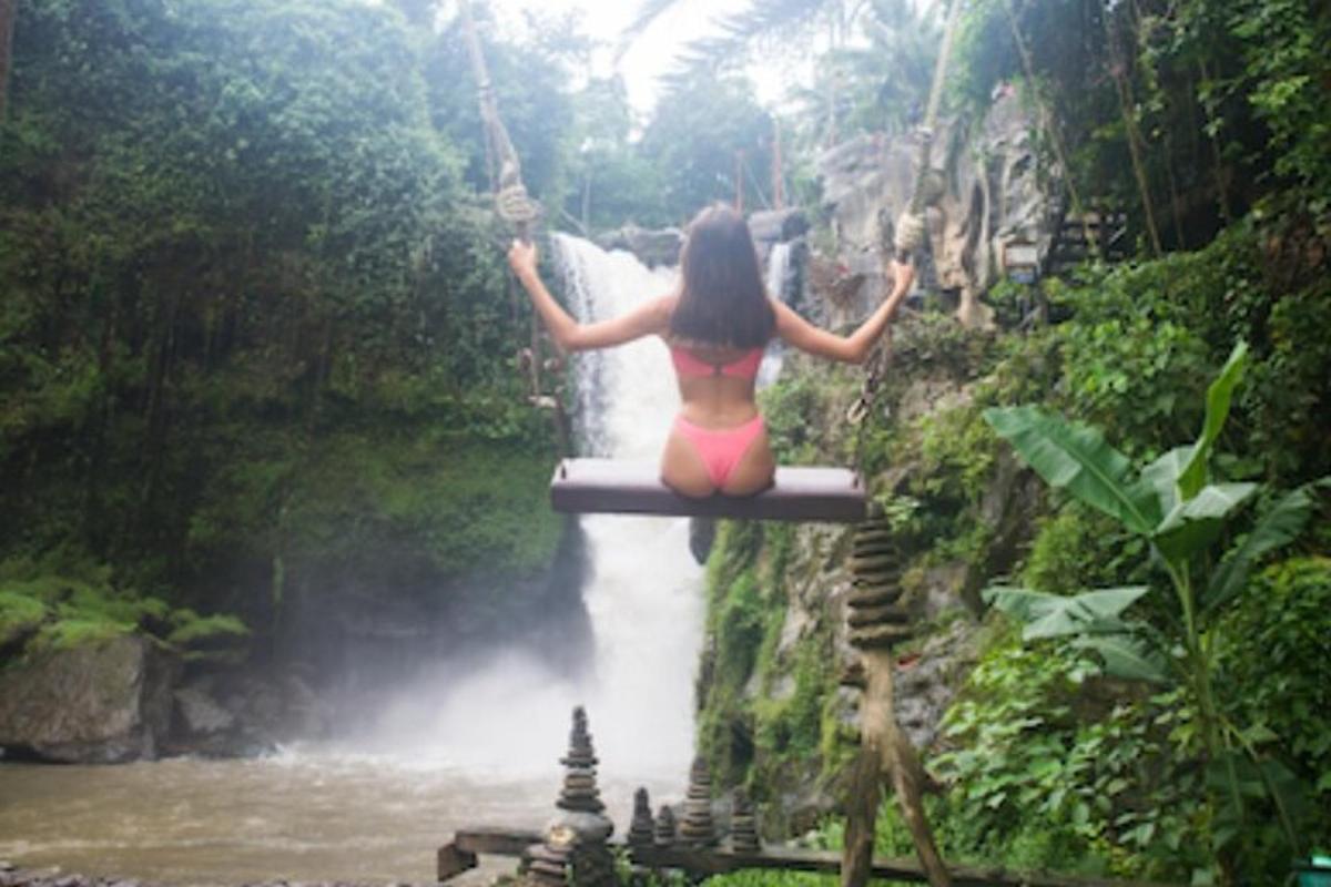 una donna in bikini seduta su un'altalena sopra una cascata