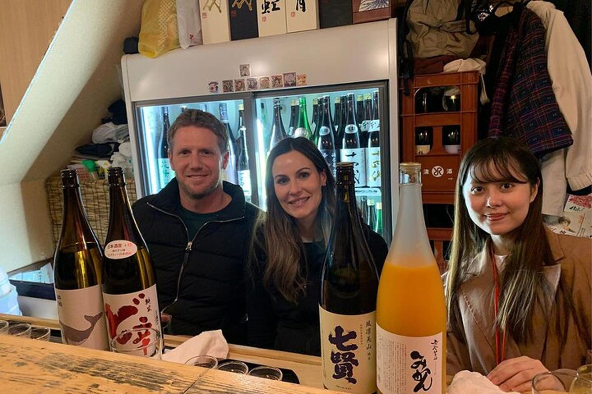 three people sitting at a bar with bottles of wine