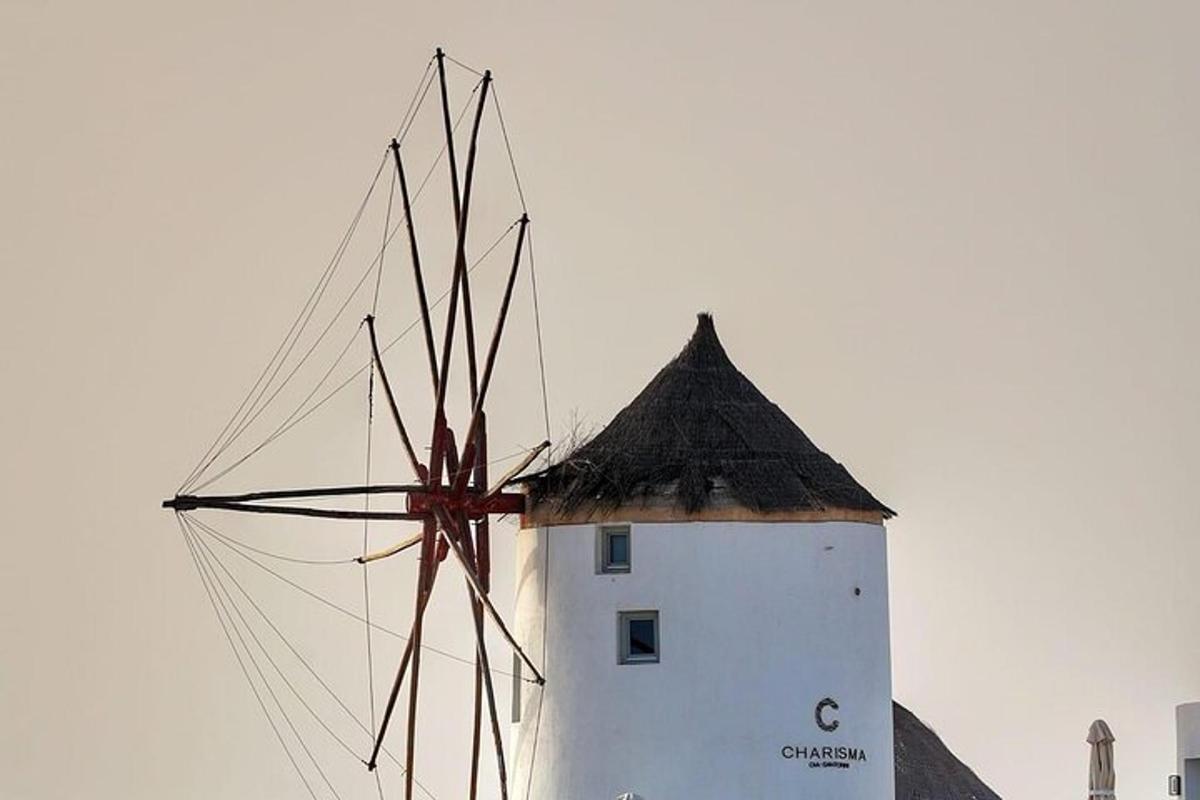 Un faro blanco con un molino de viento delante.