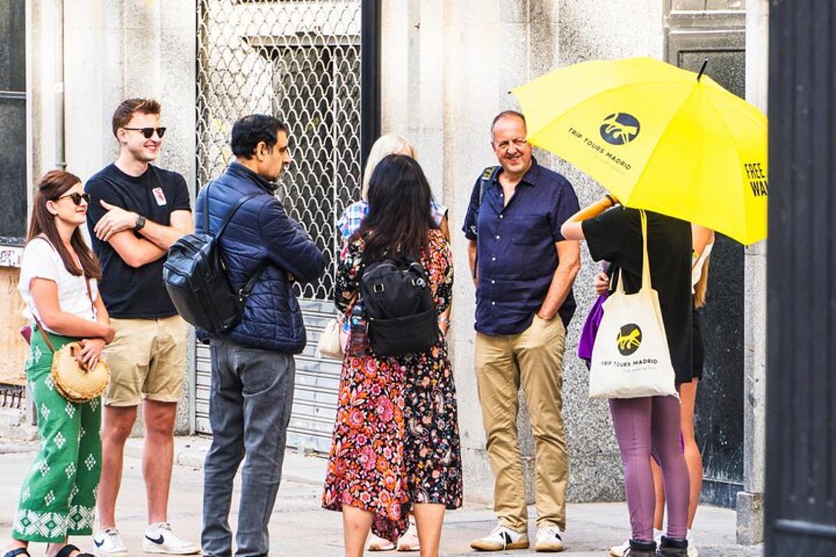 a group of people standing on a sidewalk under a yellow umbrella