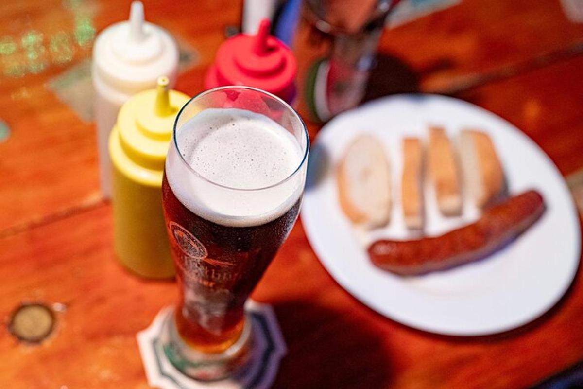 pohár piva vedľa taniera s hotdogmi