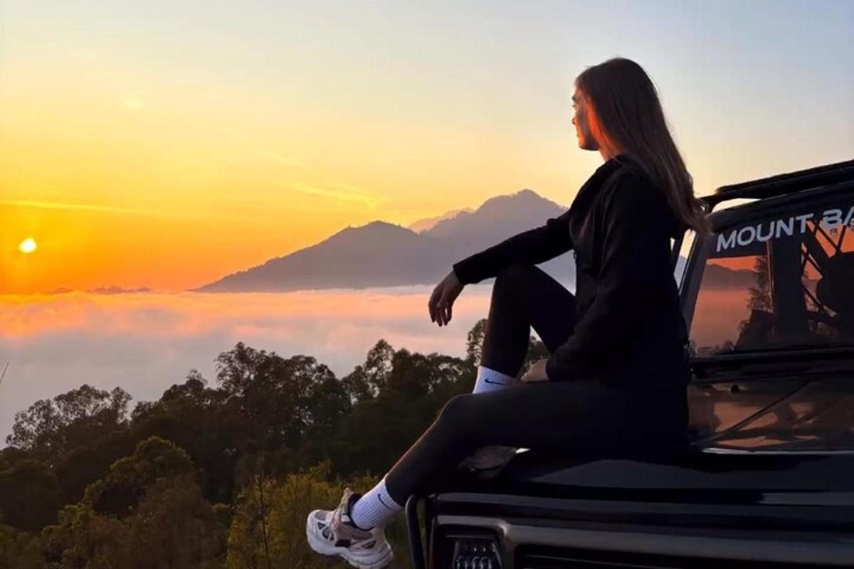 žena sedící na kapotě auta a dívající se na západ slunce