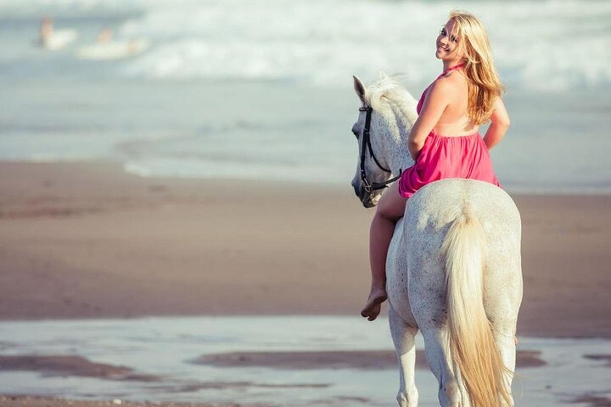 uma mulher de vestido vermelho cavalgando um cavalo branco na praia
