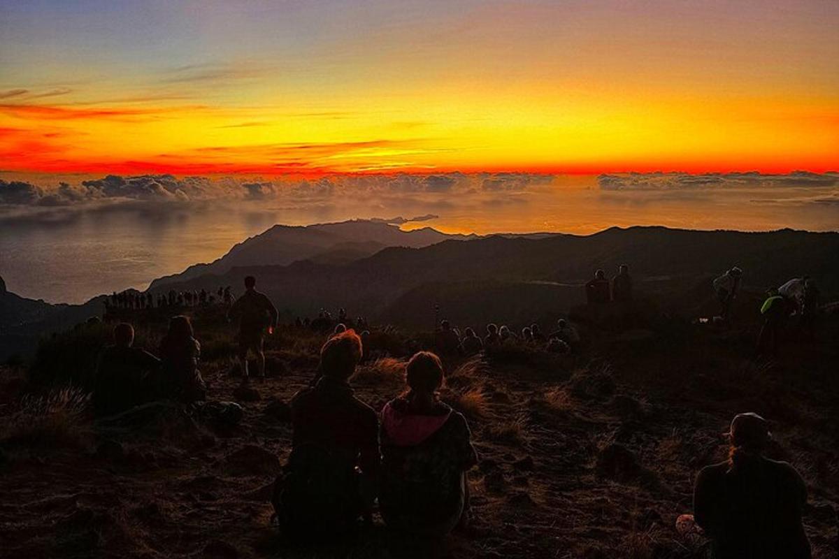um grupo de pessoas sentadas em uma montanha observando o pôr do sol