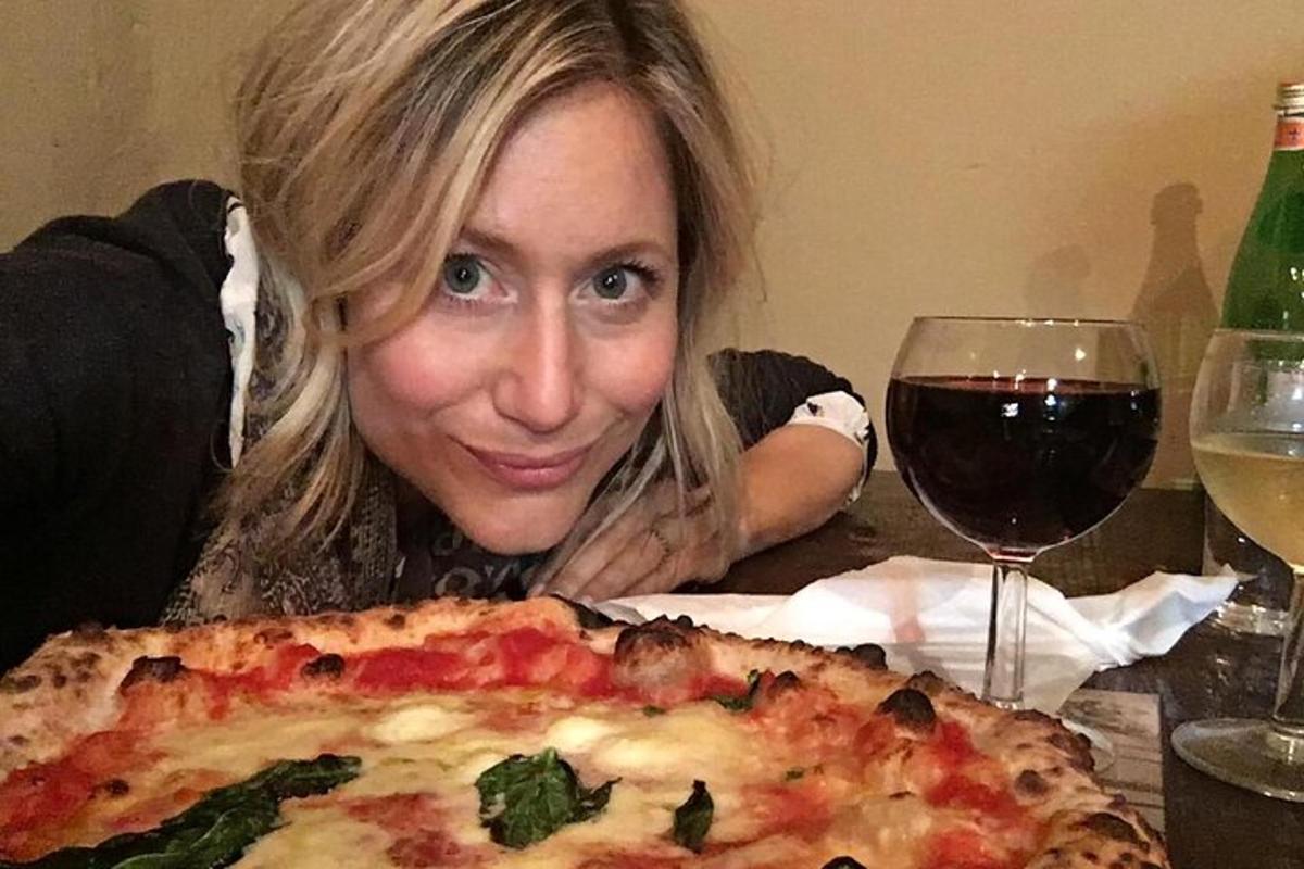 žena sedící u stolu s pizzou a sklenkou vína