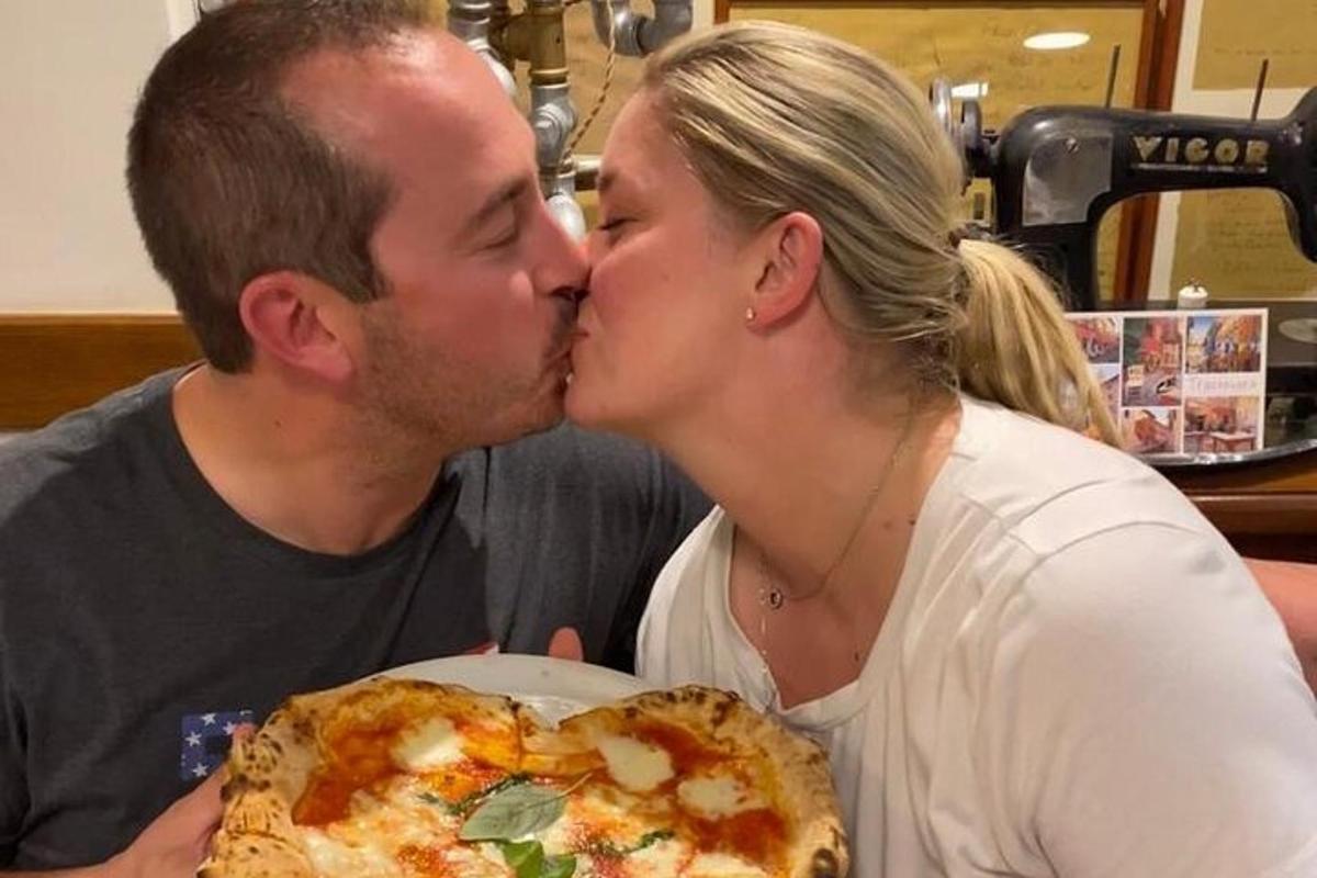 a man and a woman kissing with a pizza