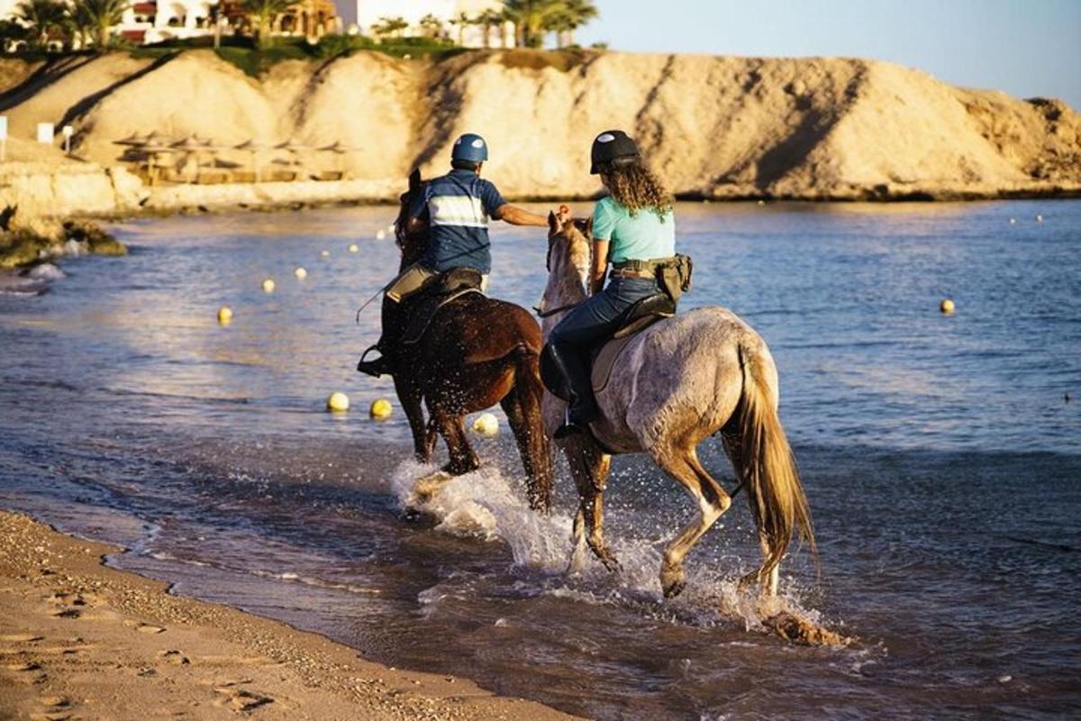due persone a cavallo nell'acqua sulla spiaggia