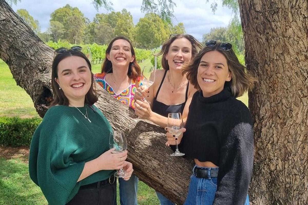 Cuatro mujeres de pie junto a un árbol sosteniendo copas de vino